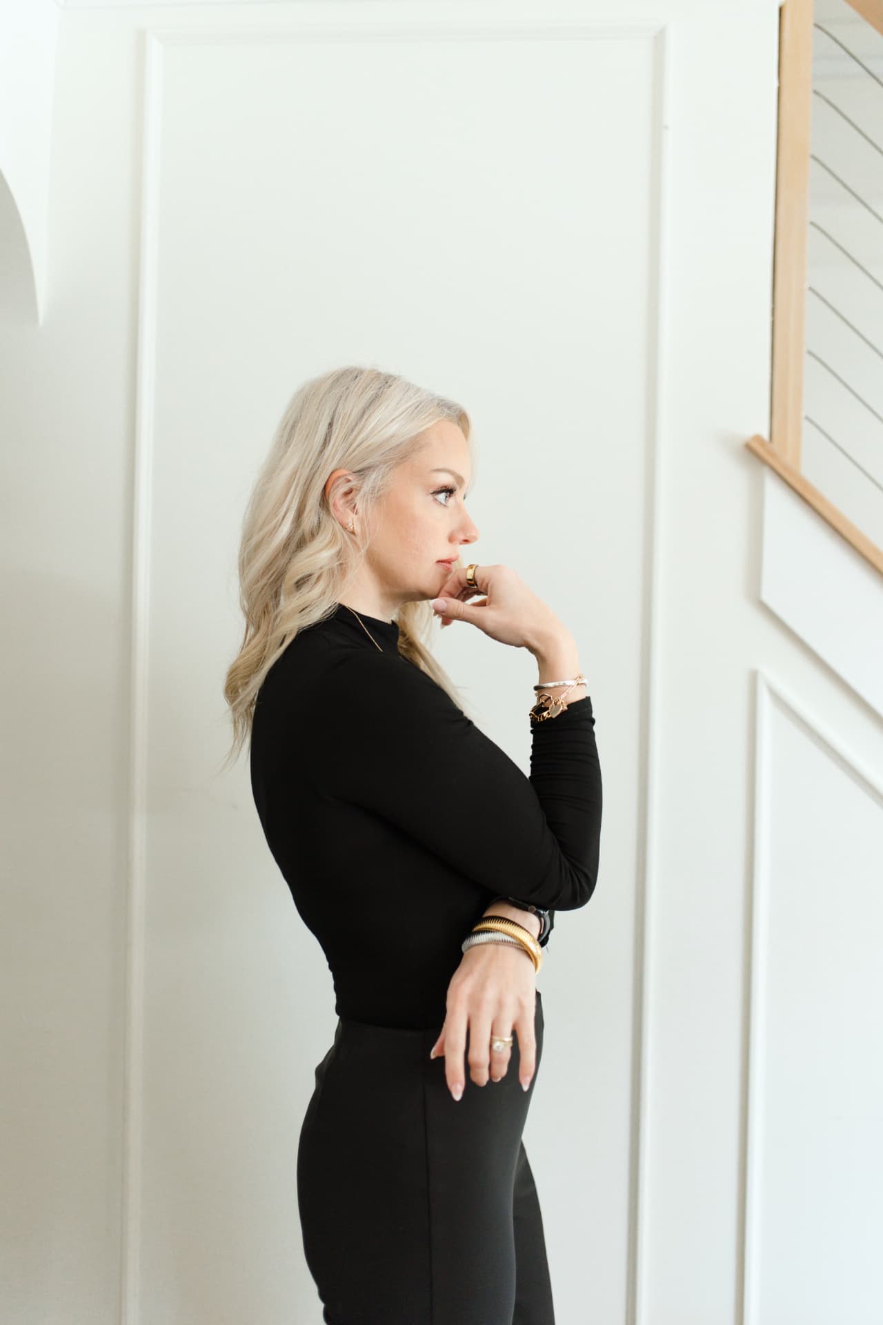 April Martini standing in profile with her hand at her chin, in front of a white paneled wall and staircase